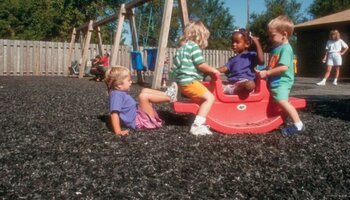 Several children playing on a toy outside in a child care setting, with a swing set in the background
