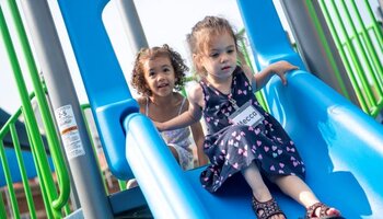 Two small girls going down a blue slide at the playground