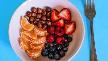 A bowl with oranges, nuts, strawberries, rasberries, and blueberries in it, with a fork to the right