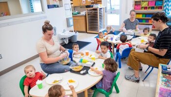 Adults eating with and overseeing children during a meal at a child care setting