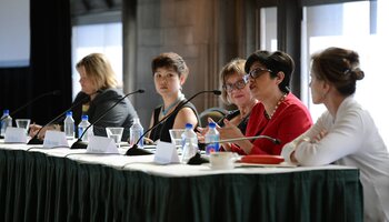 Several women at a table with microphones, serving on a panel at an academic conference