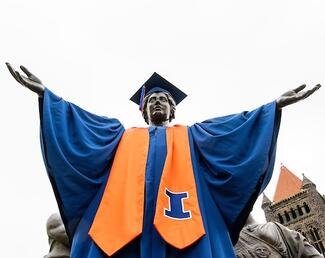 The Illinois Alma Mater statue with a blue cap and gown and orange sash